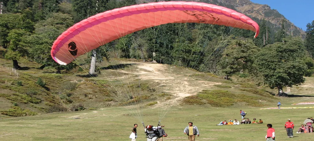 Paraglider preparing for flight in a grassy mountain meadow with spectators.