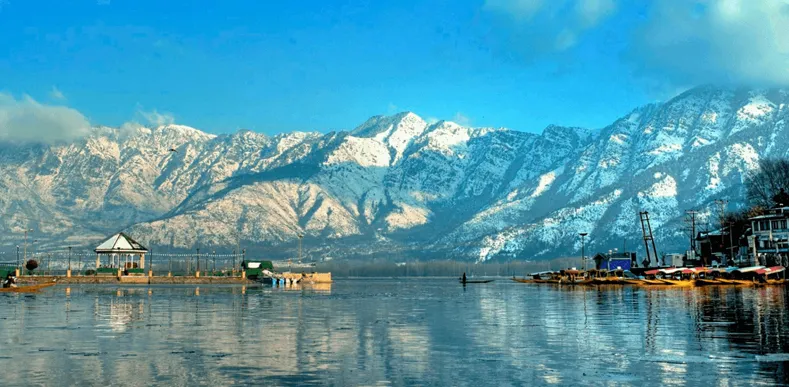 Snow-capped mountains overlook Dal Lake in Kashmir, with houseboats and a gazebo on the water.